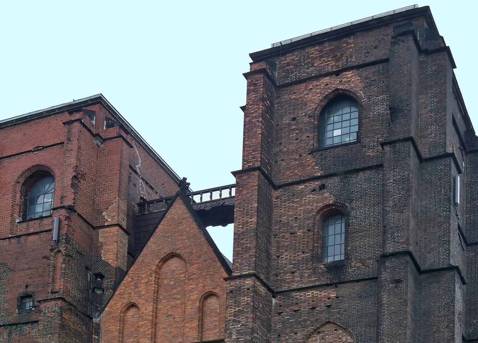 A close-up view of two connecting brick towers with arched windows, set against a light blue sky.